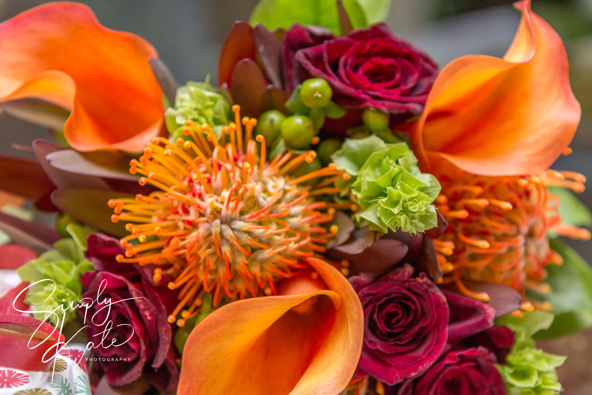 Vibrant close-up of an orange and red flower bouquet with calla lilies, roses, and green accents
